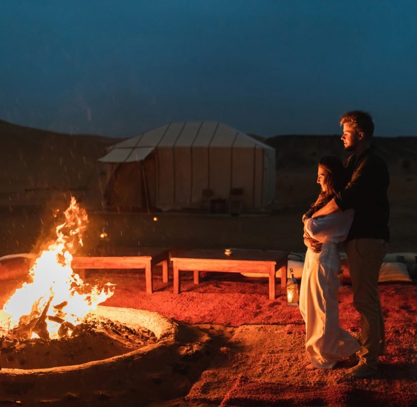 Couple hug in love near big campfire. Romantic night in glamping desert camp in Sahara, Morocco. Honeymoon.